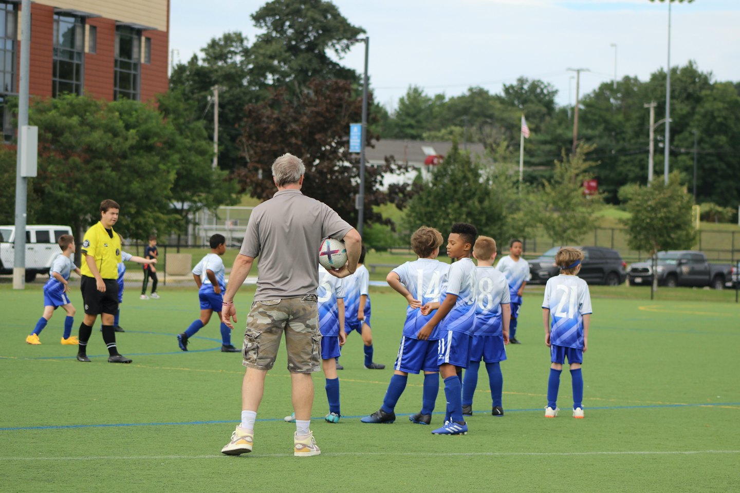 A soccer coach observes young players on an outdoor field.