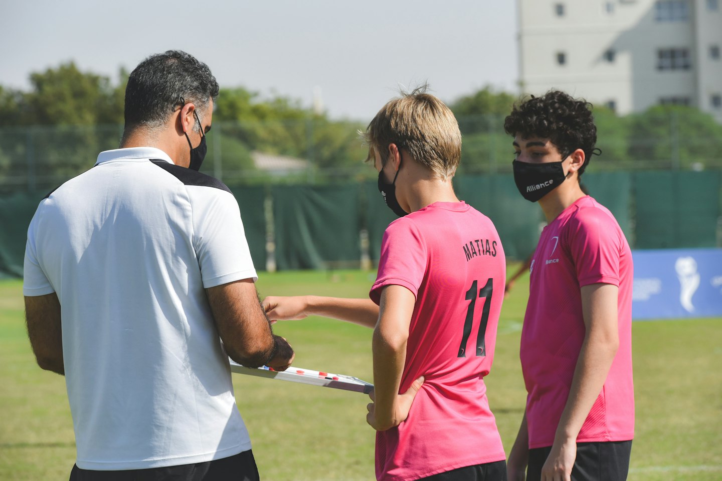 Coach instructs young athletes with a whiteboard on a sunny sports field.