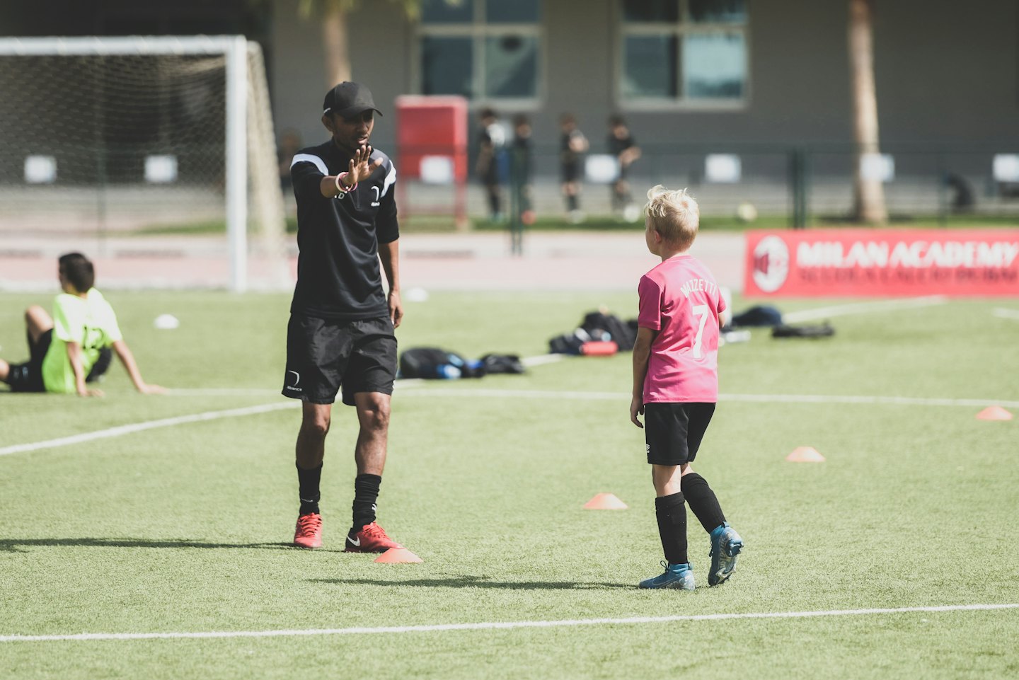 Soccer coach instructs young boy on artificial turf field.