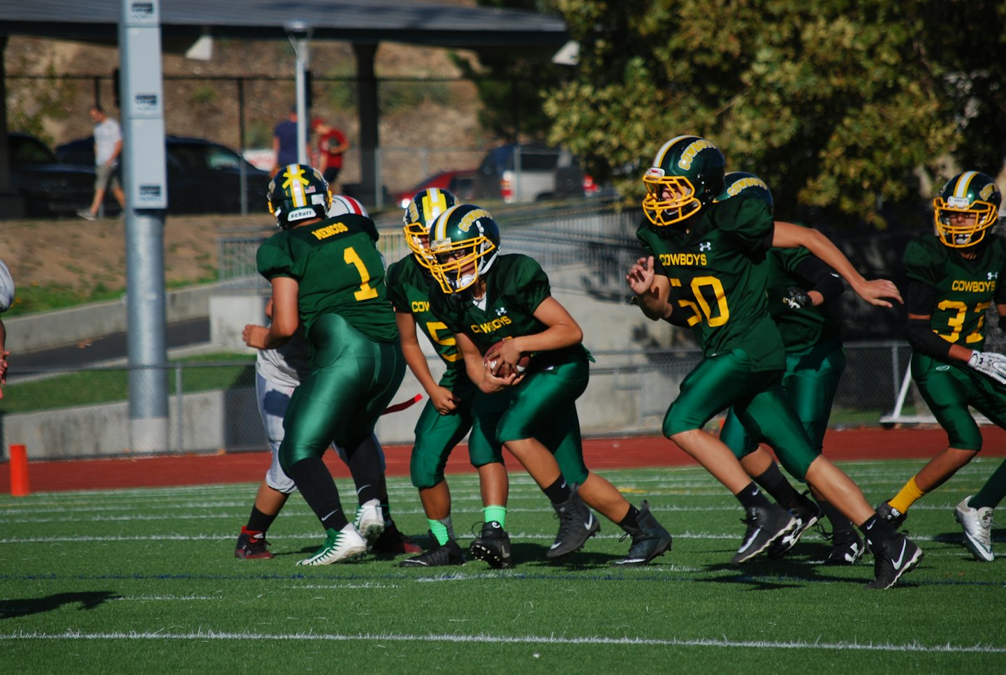 Football players in green and yellow uniforms run across a field.