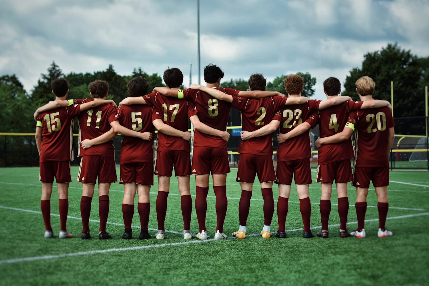 Soccer team in maroon jerseys stand together on athletic field.