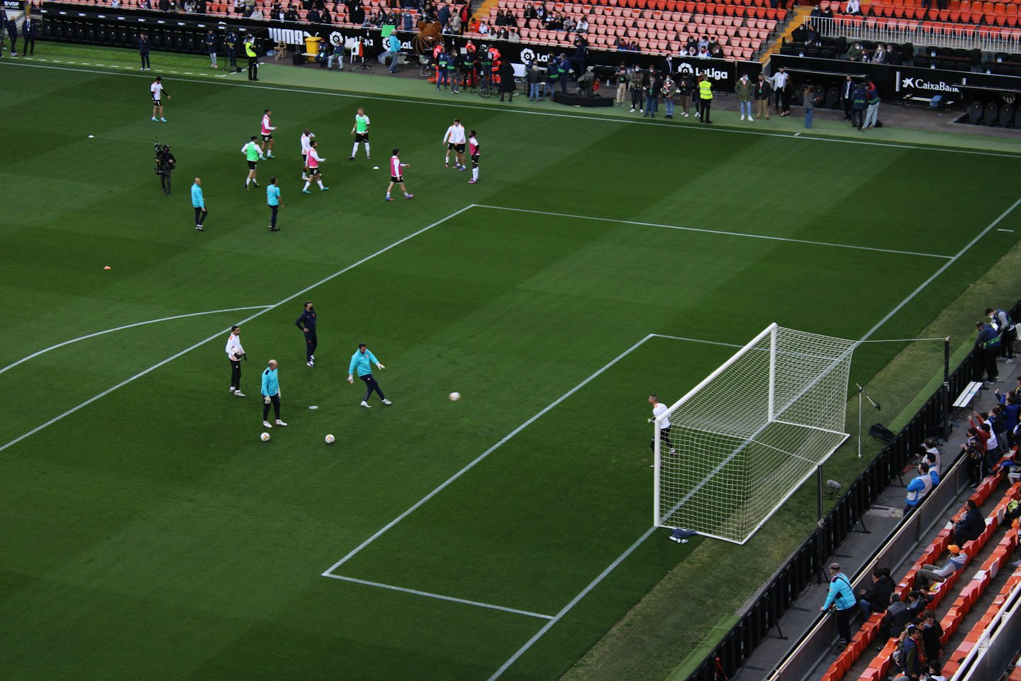 Soccer players train on a green stadium pitch near a goal.